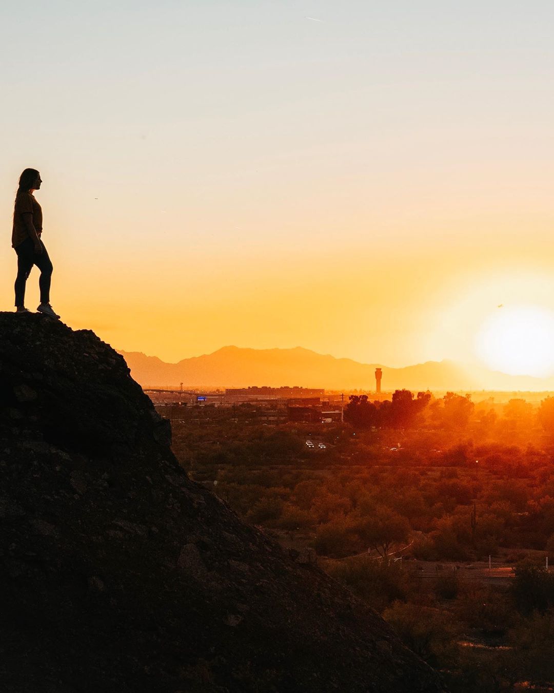 Woman Standing on Top of a Hill Overlooking Tempe at Sunset. Photo by Instagram user @throughmylensco
