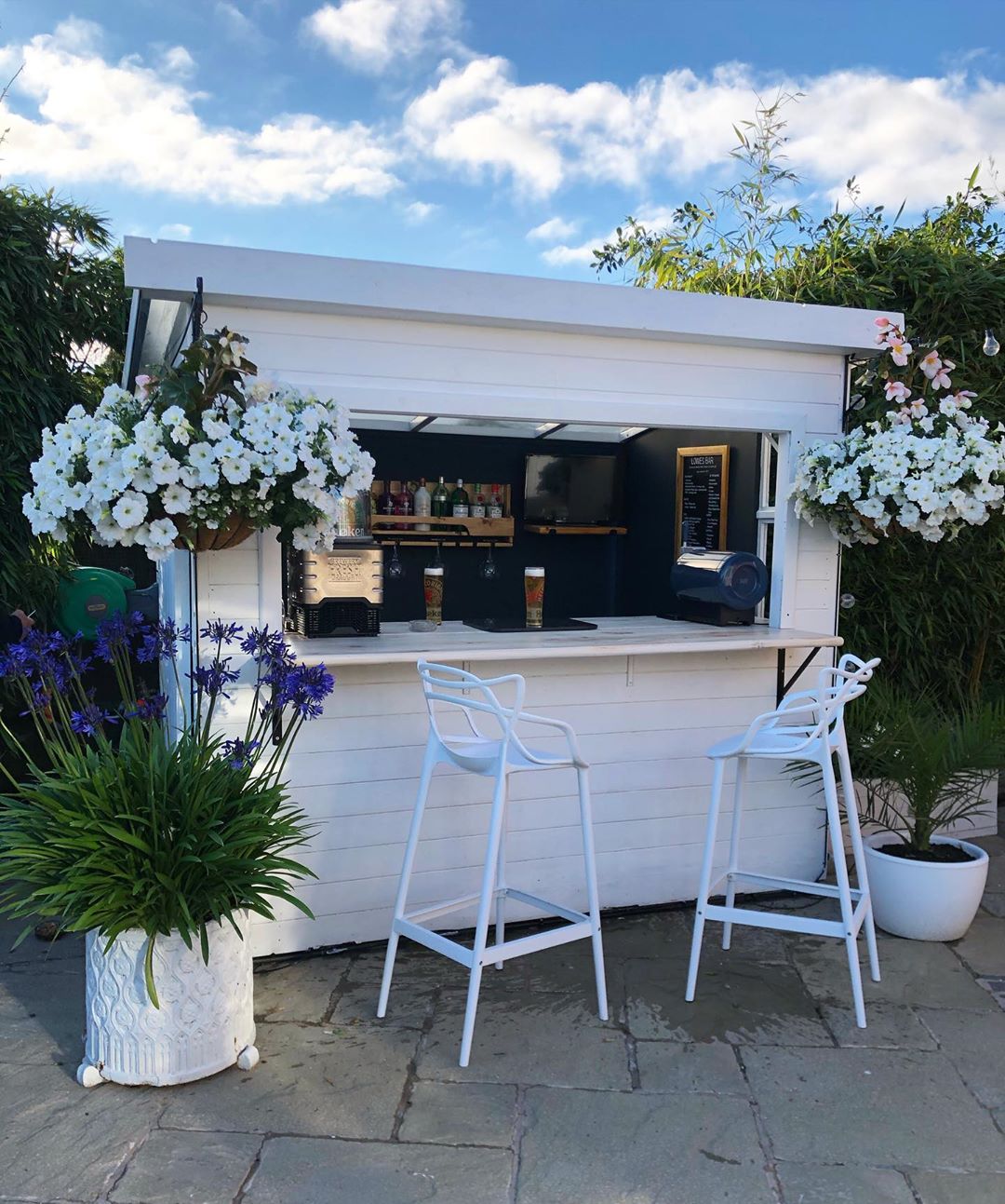 Small White Bar She Shed with White Stools in Front. Photo by Instagram user @houseonthedales