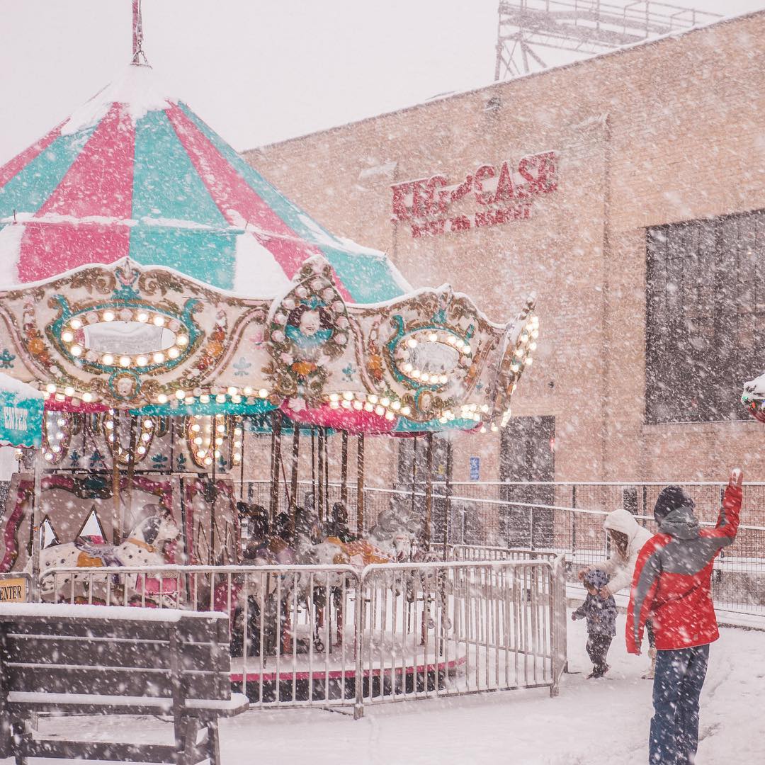 Kid Throwing a Snowball In Front of a Carousel in the Snow. Photo by Instagram user @emilyjaneandco