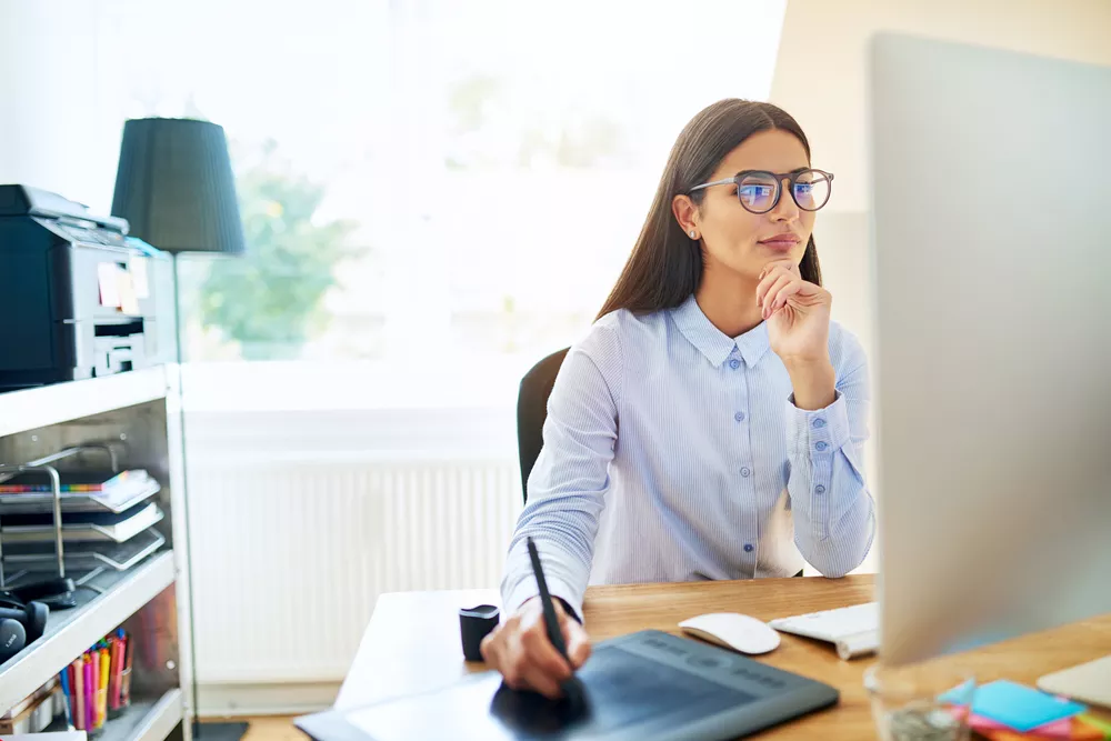 Women Wearing Glasses Sitting at a Desk Looking at a Computer Monitor