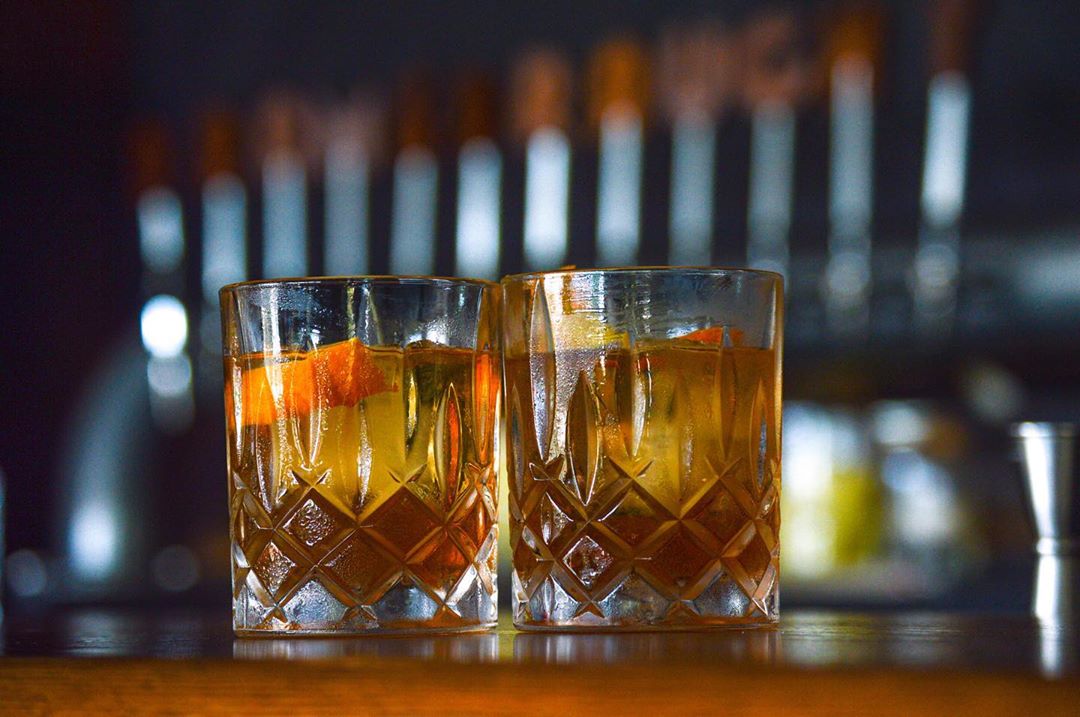 Two Old Fashioned's Sitting in Crystal Glasses on a Bar at Dram & Draught Greensboro. Photo by Instagram user @go.greensboro