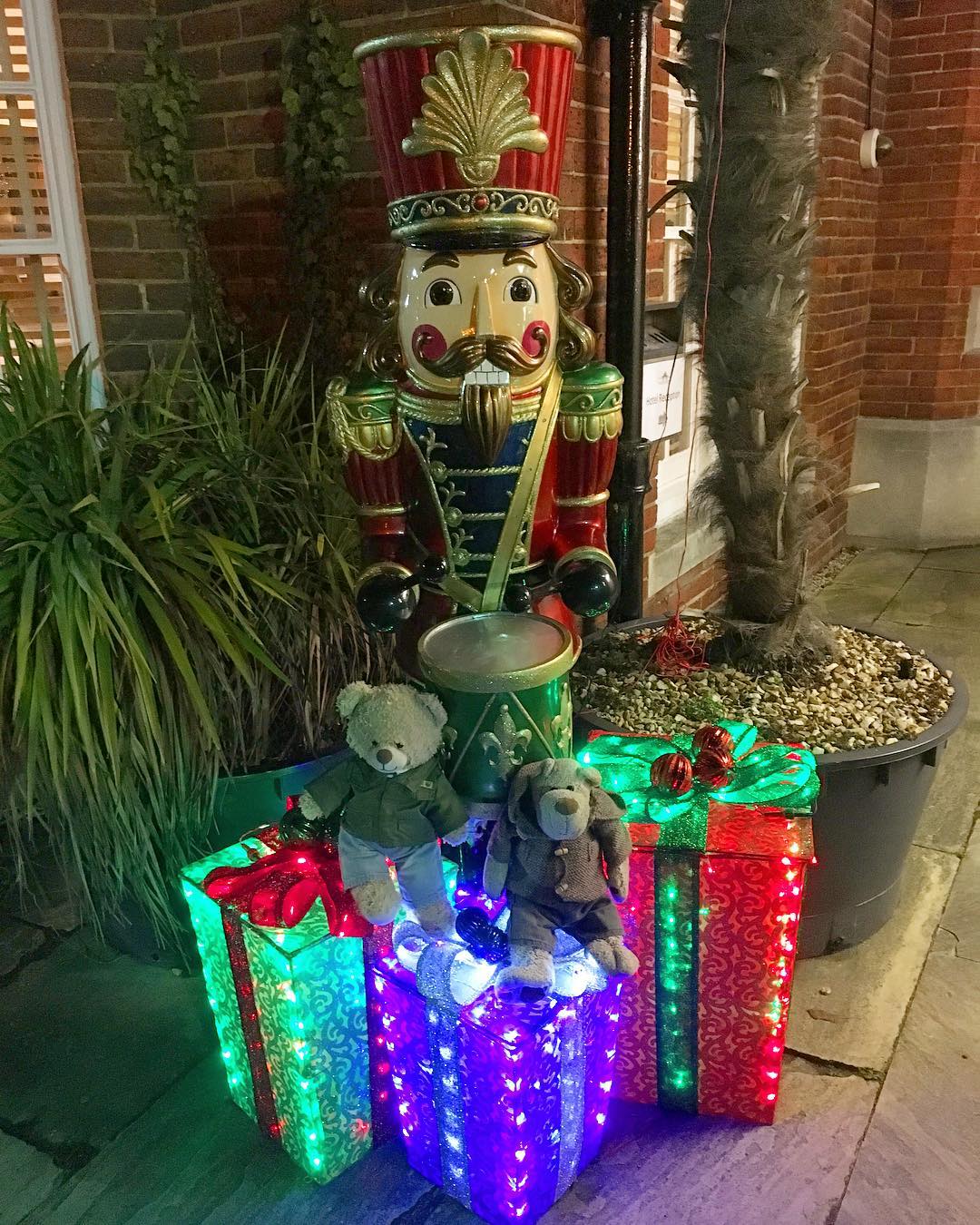 DIY presents created with a wooden frame and mesh material glow with lights outside in front of a large nutcracker. Photo by Instagram user @tedandalfiebears.