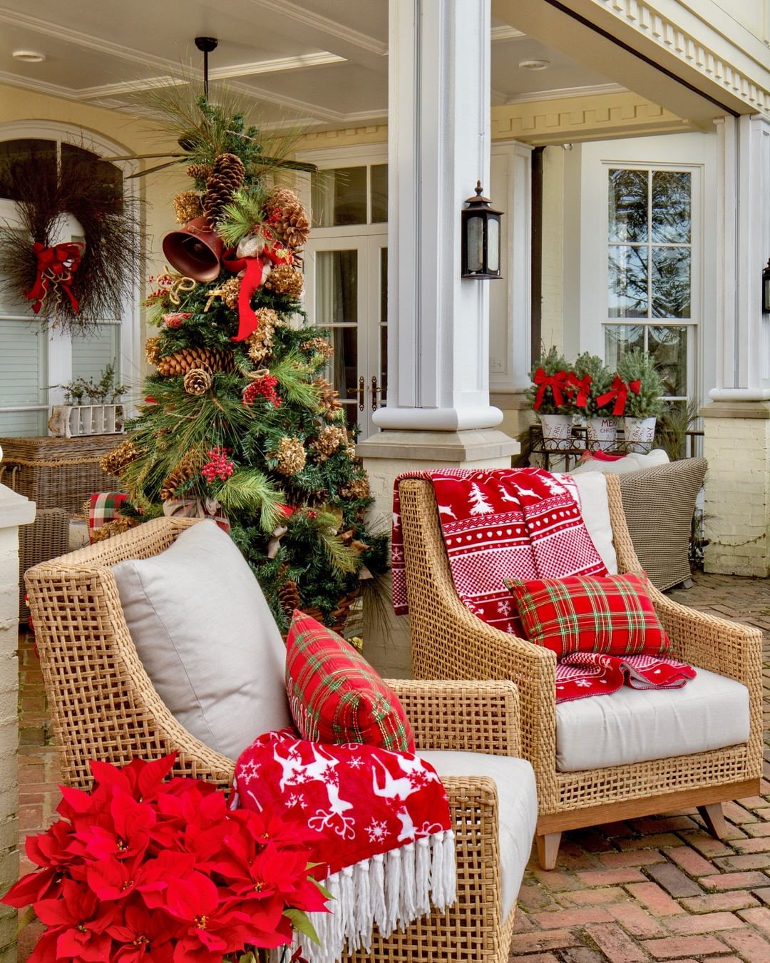Outdoor furniture chairs have red holiday pillows and a red, white, and green Christmas icon decorated blanket laid over the top of one. Photo by Instagram user @southernladymag.