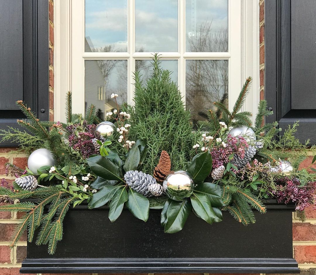 Window box stuffed with pine sprigs, cedar, cranberries, silver and regular pinecones, and gold Christmas ornaments. Photo by Instagram user @contained_creations.