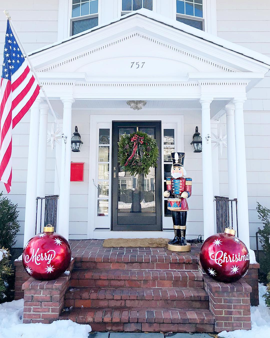 A front porch features two large DIY red ornaments saying "Merry Christmas" on either side. Photo by Instagram user @honeyandfitz.