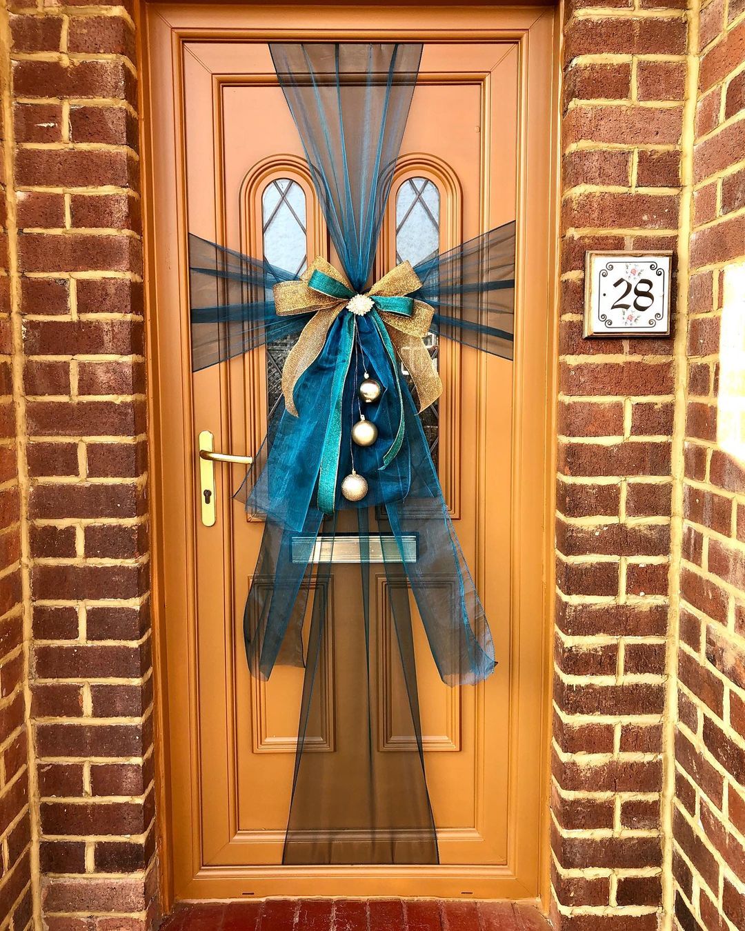 Large bows wrapping a front door with some gold ornaments hanging from the middle of the bow. Photo by Instagram user @flowersbyjemmaholmes.