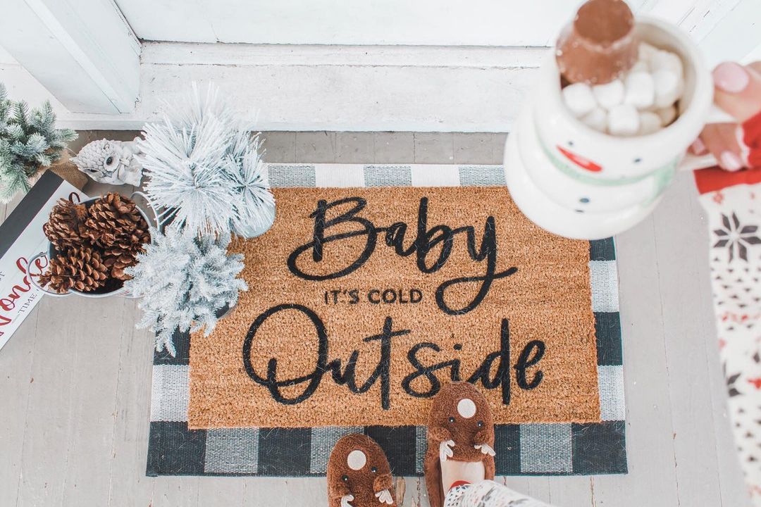 Coconut welcome mat on the front porch with the song title "Baby, It's Cold Outside" written in cursive. Photo by Instagram user @molly.elizabeth.foster.