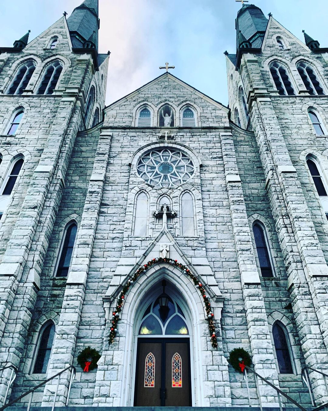Sacred Heart Parish imposing against the sky, with garland around the entrance doorframe and a wreath on either side of the entry. Photo by Instagram user @travelwithlove.usa.