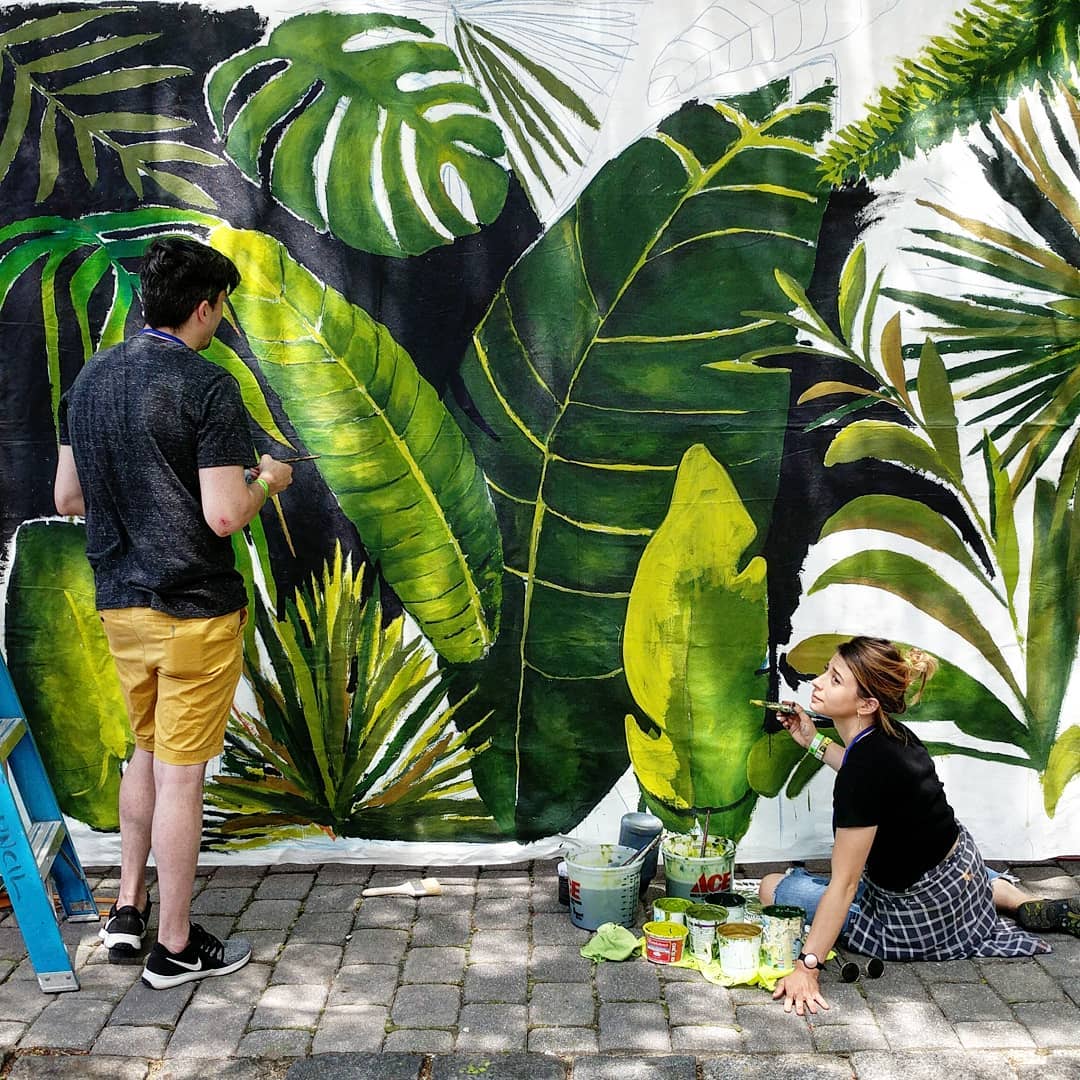 An artist speaking to a helper as she finishes her jungle mural. Photo by Instagram user @ckennylin