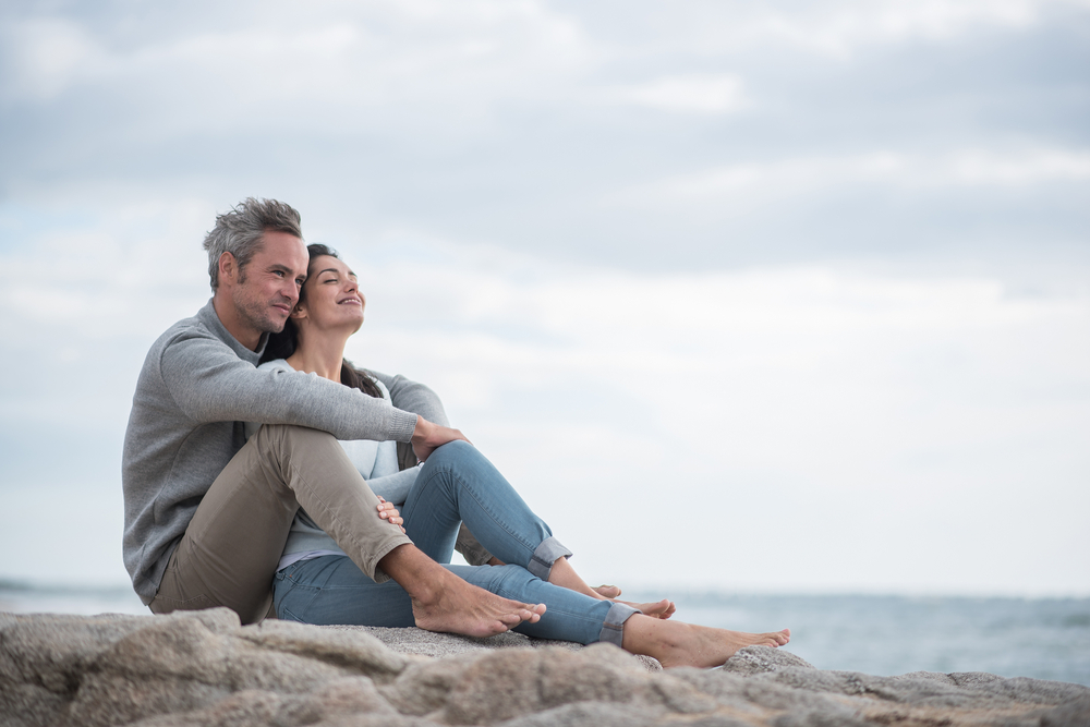 Man and Woman Sitting By the Sea Holding One Another