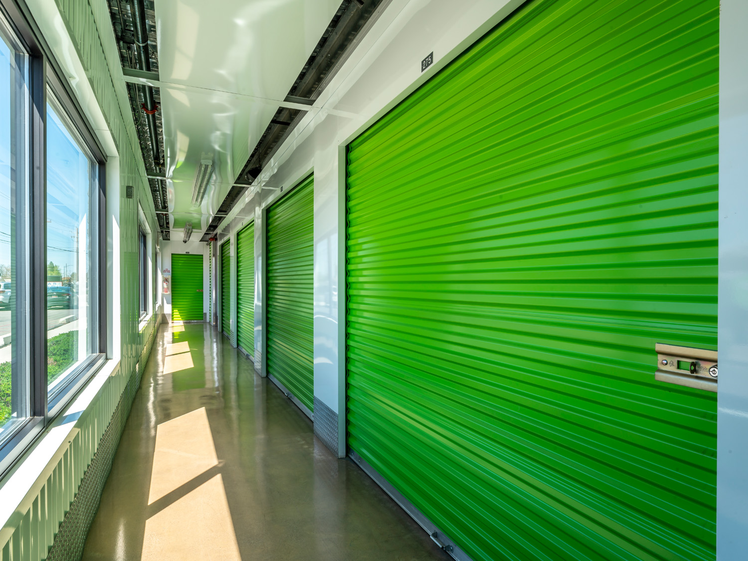 View down a hallway of an Extra Space Storage facility; hallways is clean, well-lit, and has bright green garage-like doors