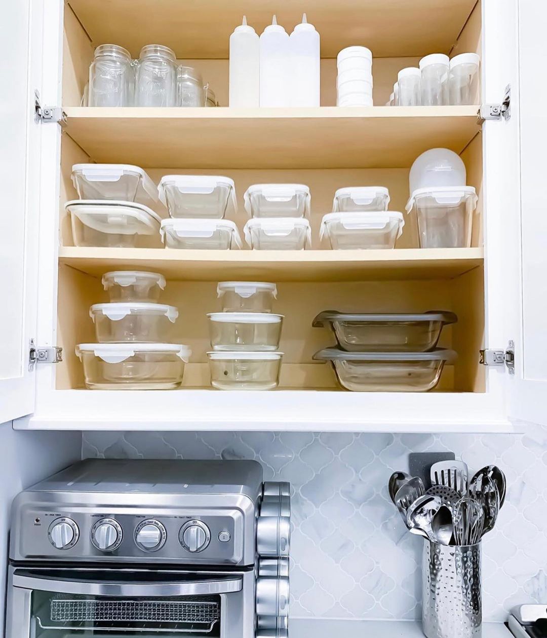 Open kitchen cabinet with tupperware containers stacked tidily. Photo by Instagram user @simplify_with_steph.
