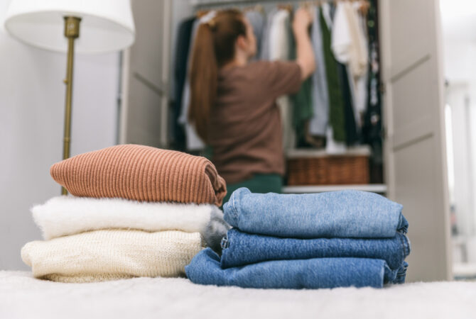 Woman Putting Clothes Away in a Closet with Folded Clothes on the bed