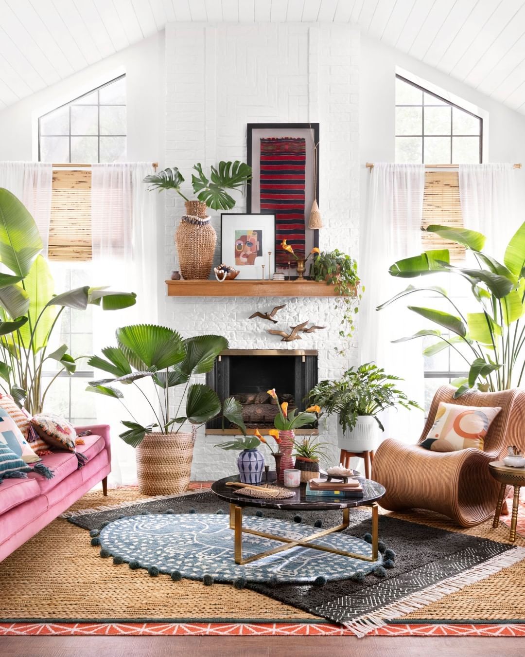 White living room with a fireplace, lots of plants, and furniture on an outdoor rug, an additional, softer rug atop it, and a circular blue-and-white patterned rug above that one, under the coffee table. Photo by Instagram user @rugs.shop.