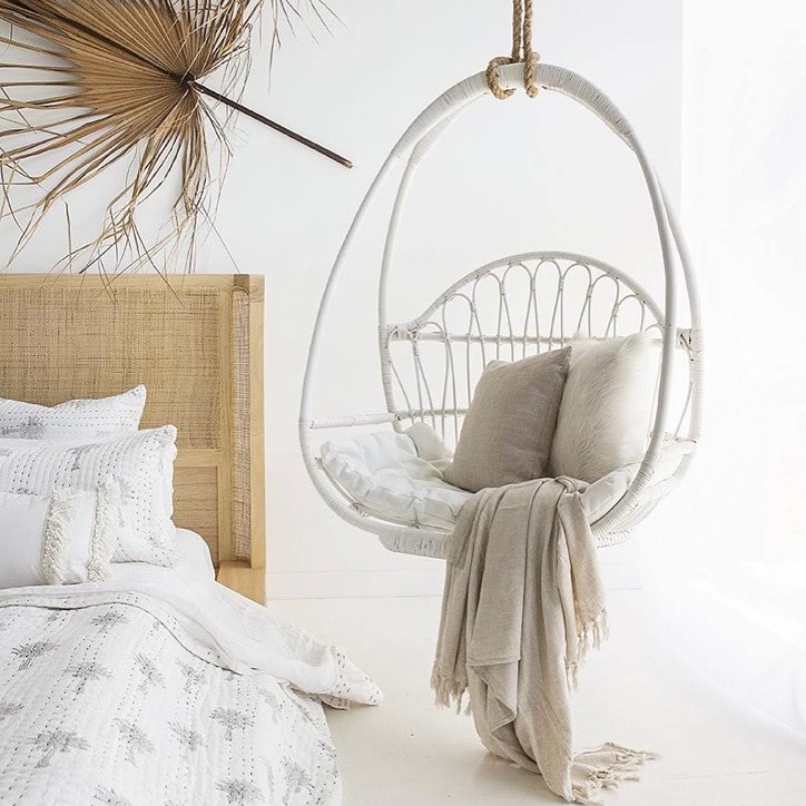White rattan hanging chair in a bright, Bohemian style bedroom. Photo by Instagram user @cabana_sanctuarycove