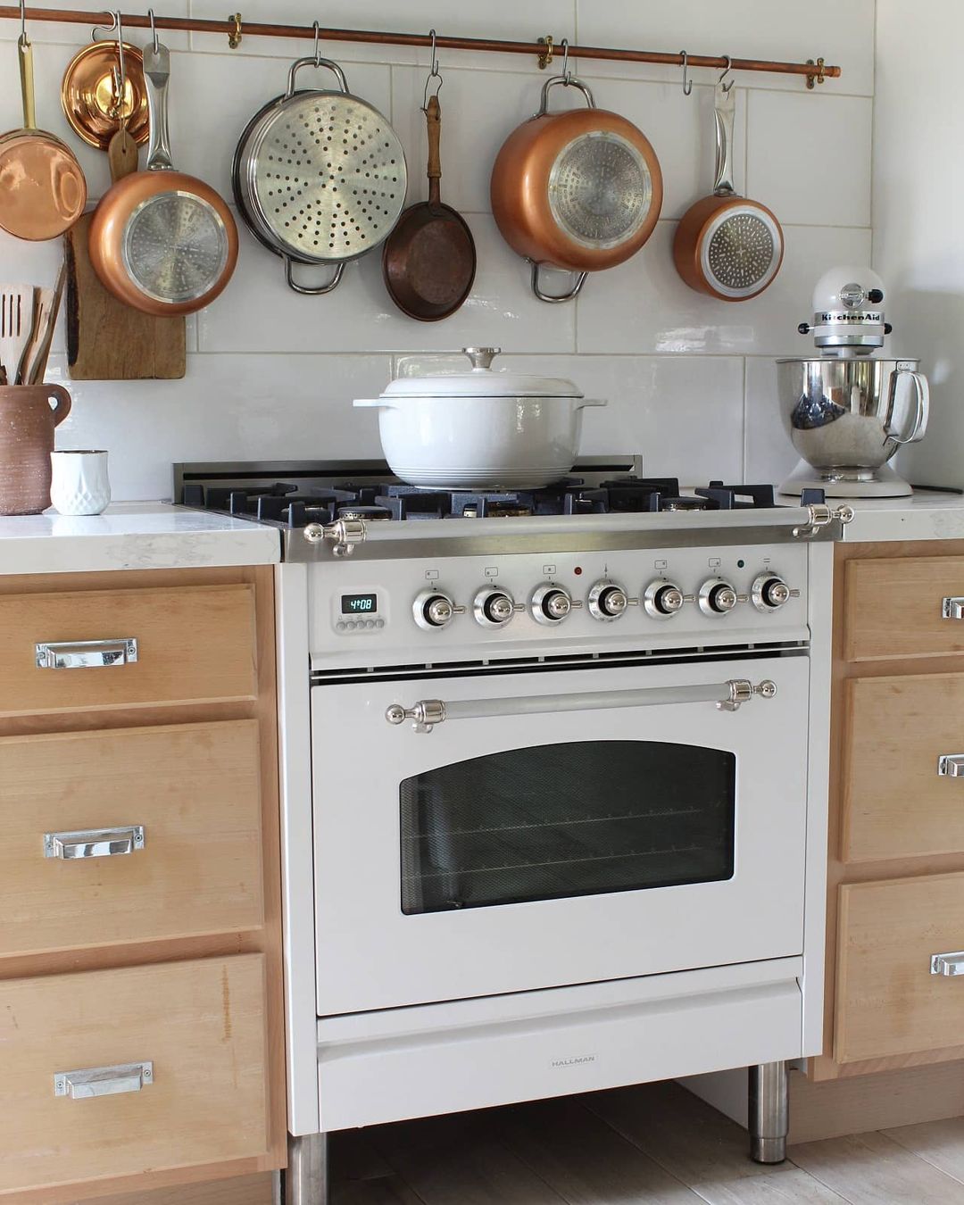Stovetop with white pot and other pans hung on backsplash. Photo by Instagram user @thevintagebucket