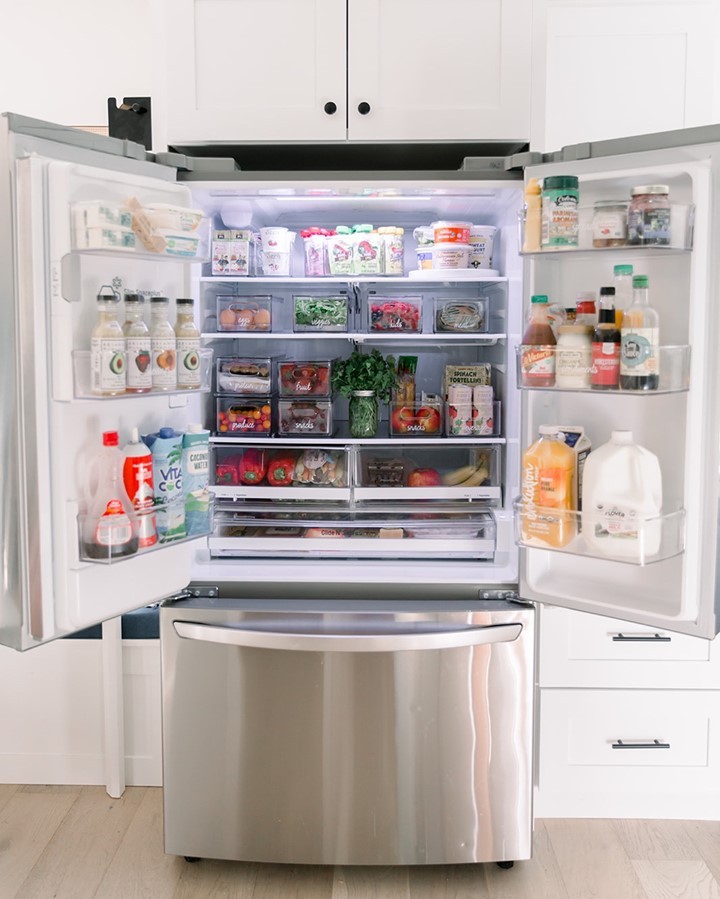 Open fridge organized using clear plastic bins. Photo by Instagram user @simplyorganizedco
