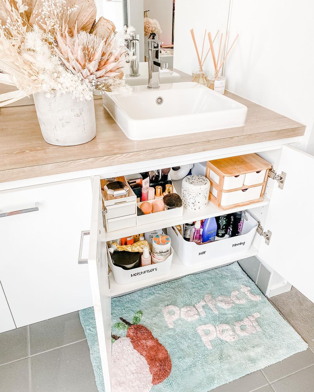 Under-the-sink doors are open to reveal a clean and organized storage area. Photo by Instagram user @ashleejayinteriors.