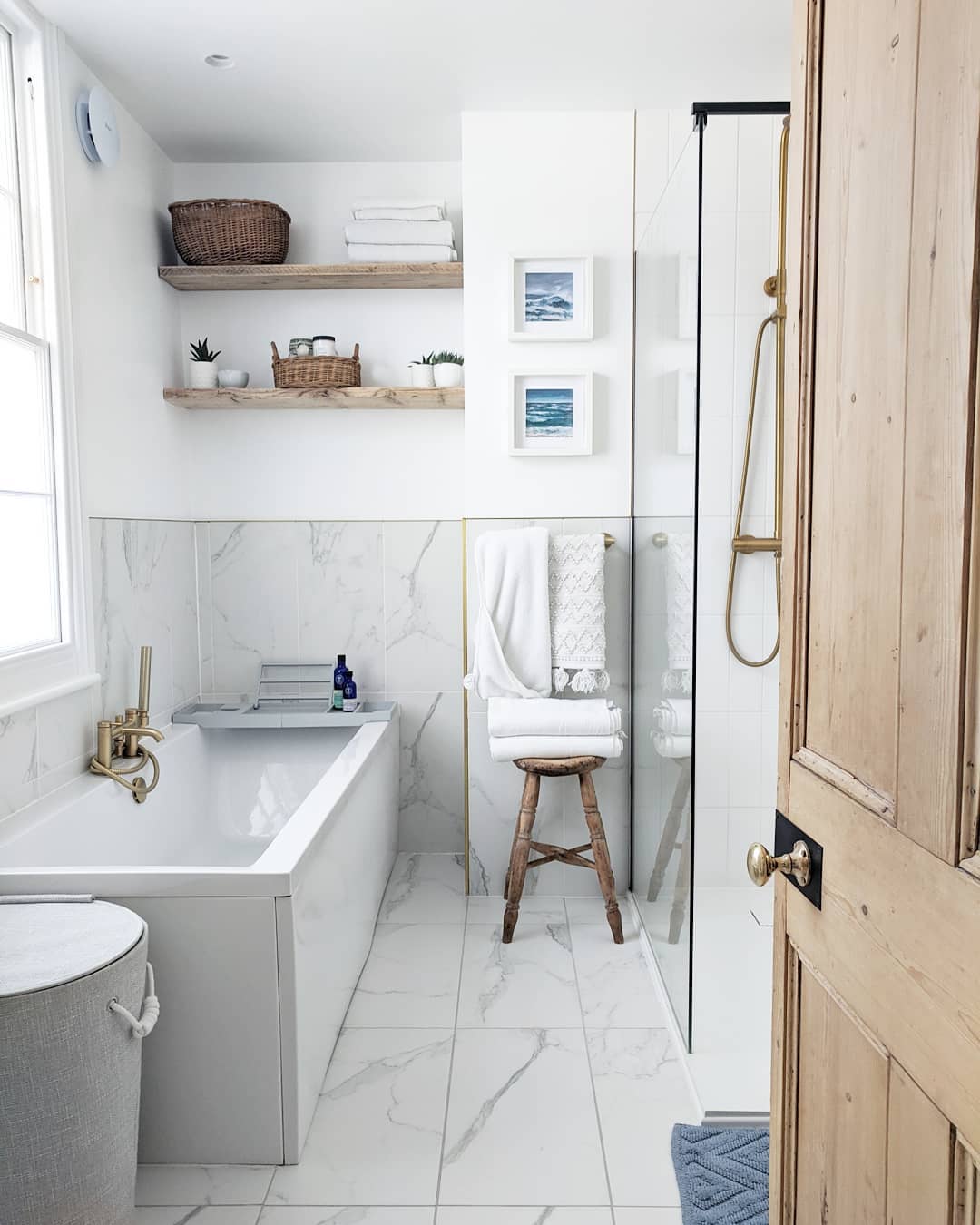 Marble bathroom featuring a stand-up shower, bathtub, shelves, and an exhaust fan. Photo by Instagram user @elizabethdanoninteriortherapy.