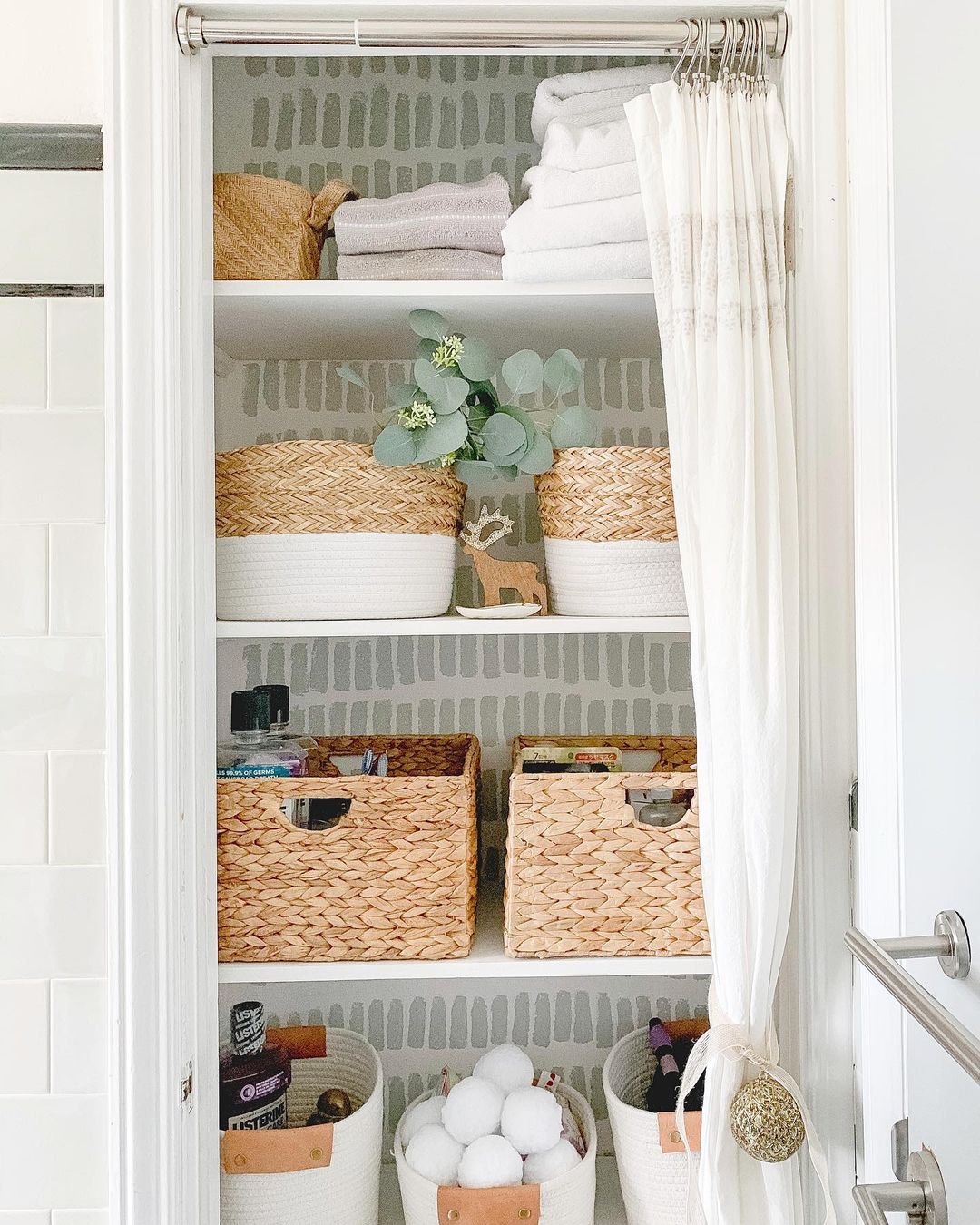 Linen closet in a bathroom featuring woven baskets to store various bathroom supplies, including towels, mouthwash, and other various objects not seen. Photo by Instagram user @lbowhome.