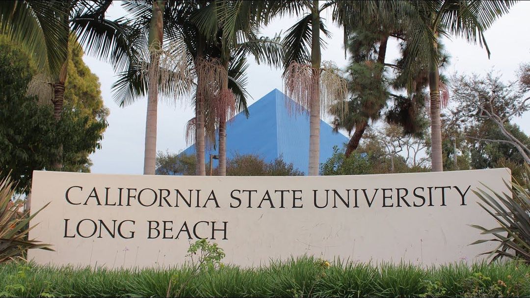 California State University Long Beach sign presented in the foreground, with palms in the middle, and the pyramid in the distance. Photo by Instagram user @csulb.24.