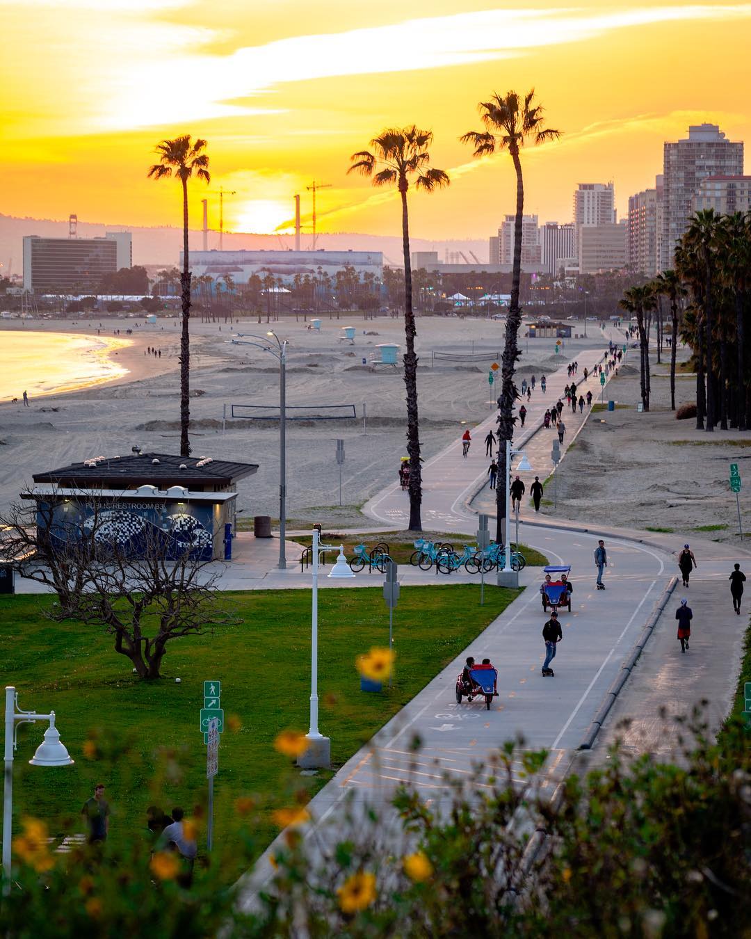 Golden hour photo of the boardwalk of Long Beach, CA, with skaters, bikers, riders, and pedestrians. Photo by Instagram user @bigdawg_manny.