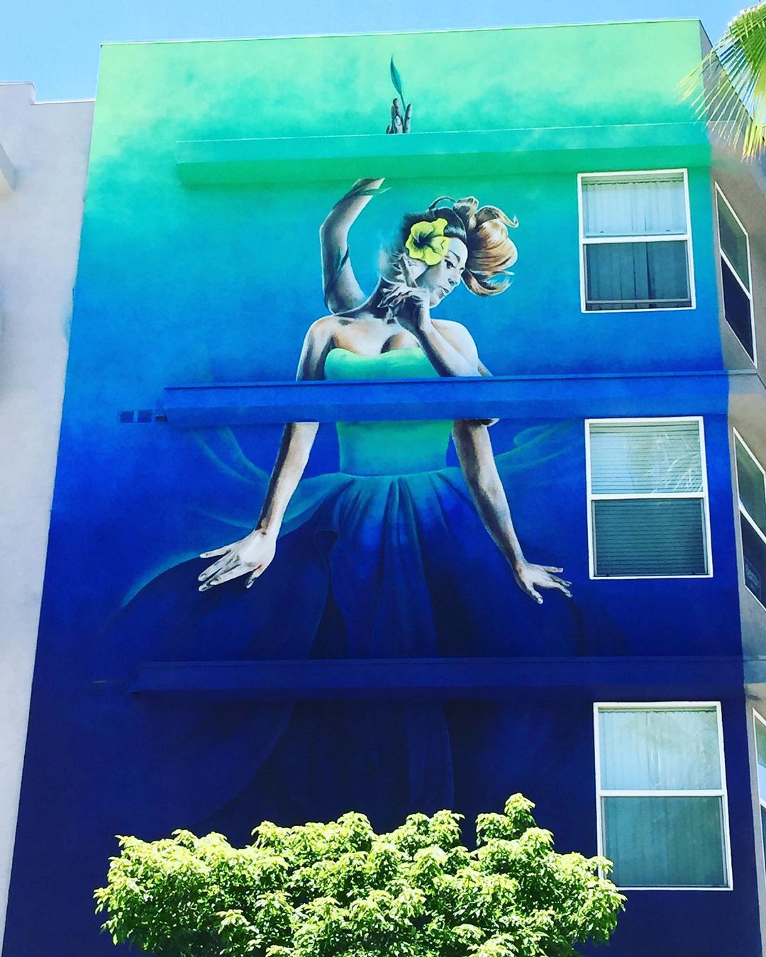 One of the many murals dispersed throughout the Long Beach metro, featuring a young woman with four arms, a flower, a vine, and a flowy dress. Photo by Instagram user @thepursuitofhappenstance.