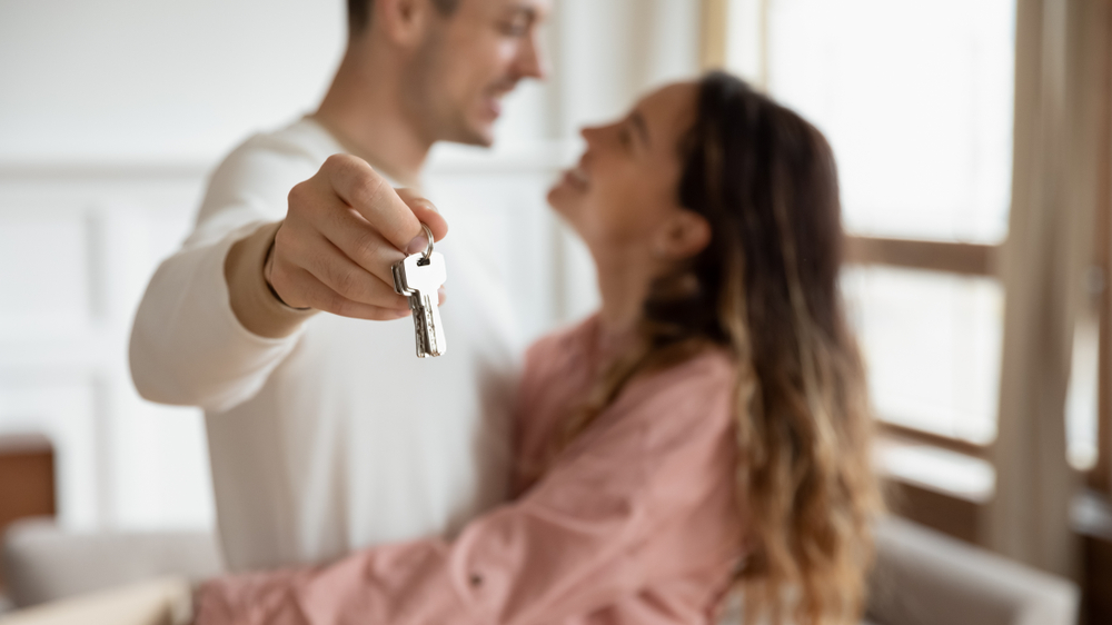 Happy couple hugs and holds keys to their new home.