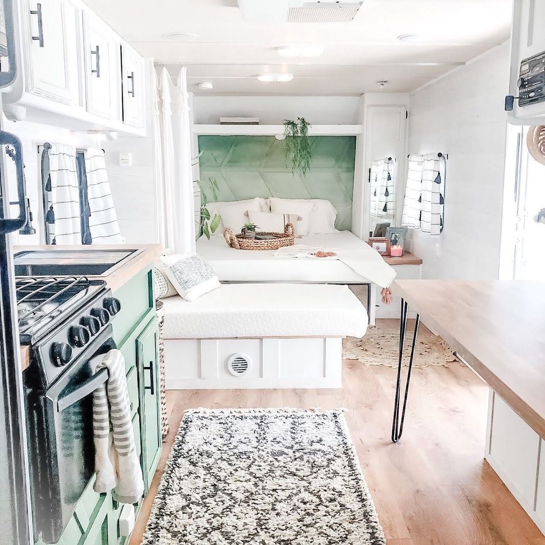 Down the long side of an RV, view of large and small beds with hidden storage, cabinets, stove and sink, and table. Photo by Instagram user @rv.family.reno.