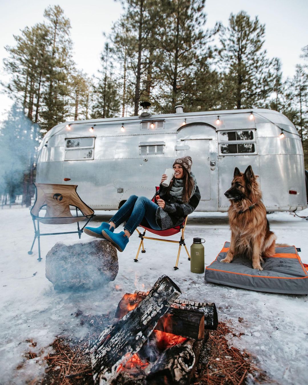 Woman Sitting Outside of a Airstream with her Dog Around the Campfire. Photo by Instagram user @briskventure