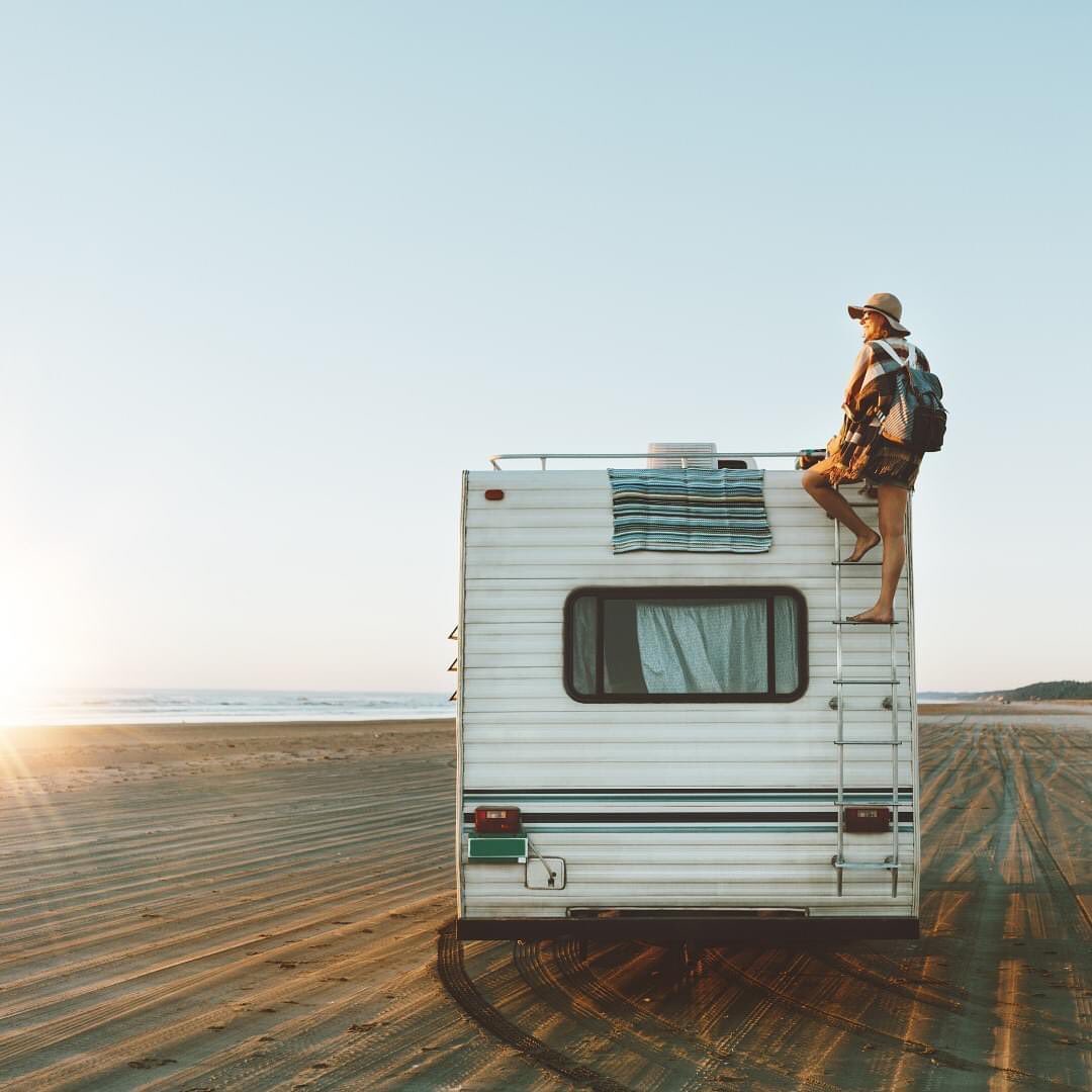 Woman Climbing the Ladder on the Back of an RV on the Beach. Photo by Instagram user @poprvs