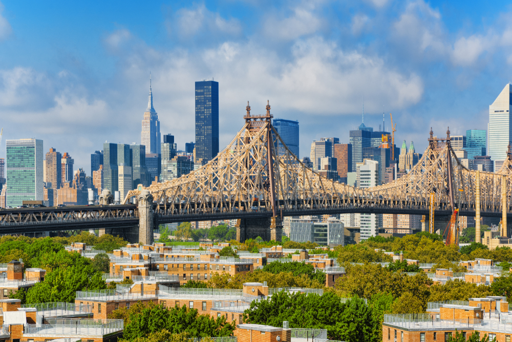 NYC skyscrapers and Queensboro bridge behind shorter trees and buildings on sunny day