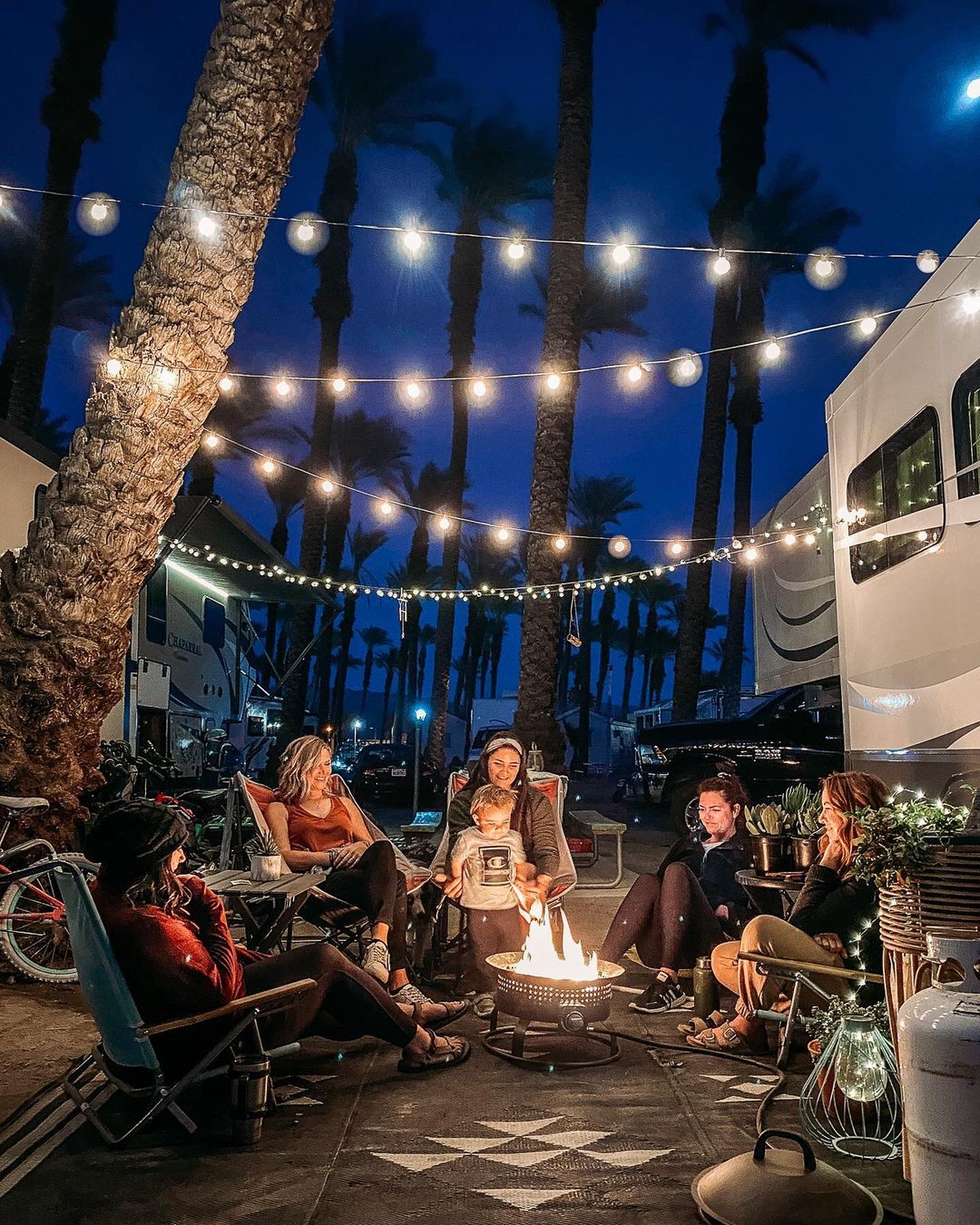 Group of people gathered around a fire pit in an RV park. Photo by Instagram User @the.wanderpreneurs