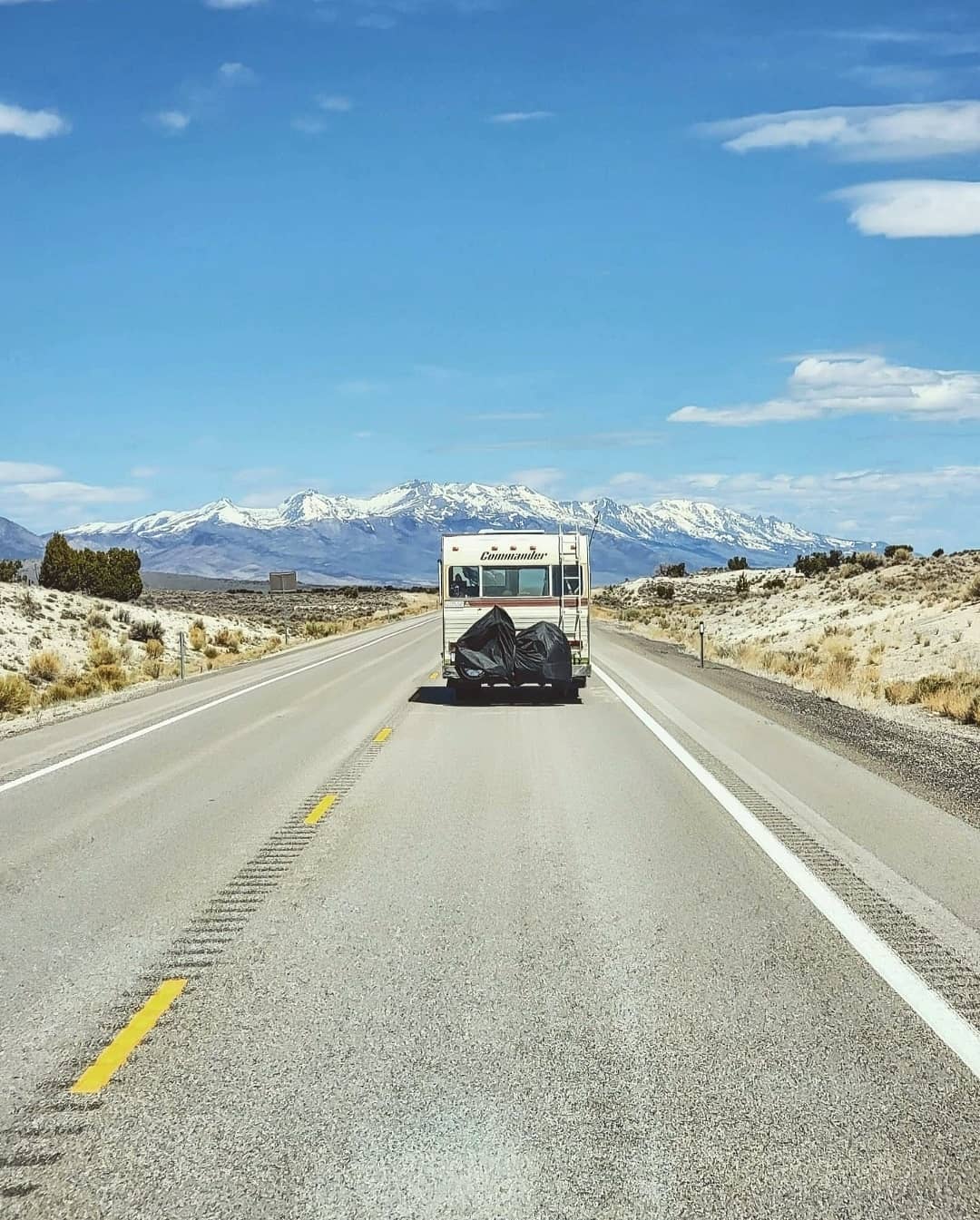 RV on the road with mountains in the background. Photo by Instagram user @a.girl.and.her.commander
