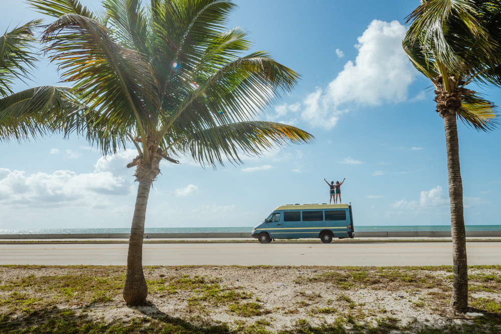 Two People Standing On top of an RV in Front of the Coast