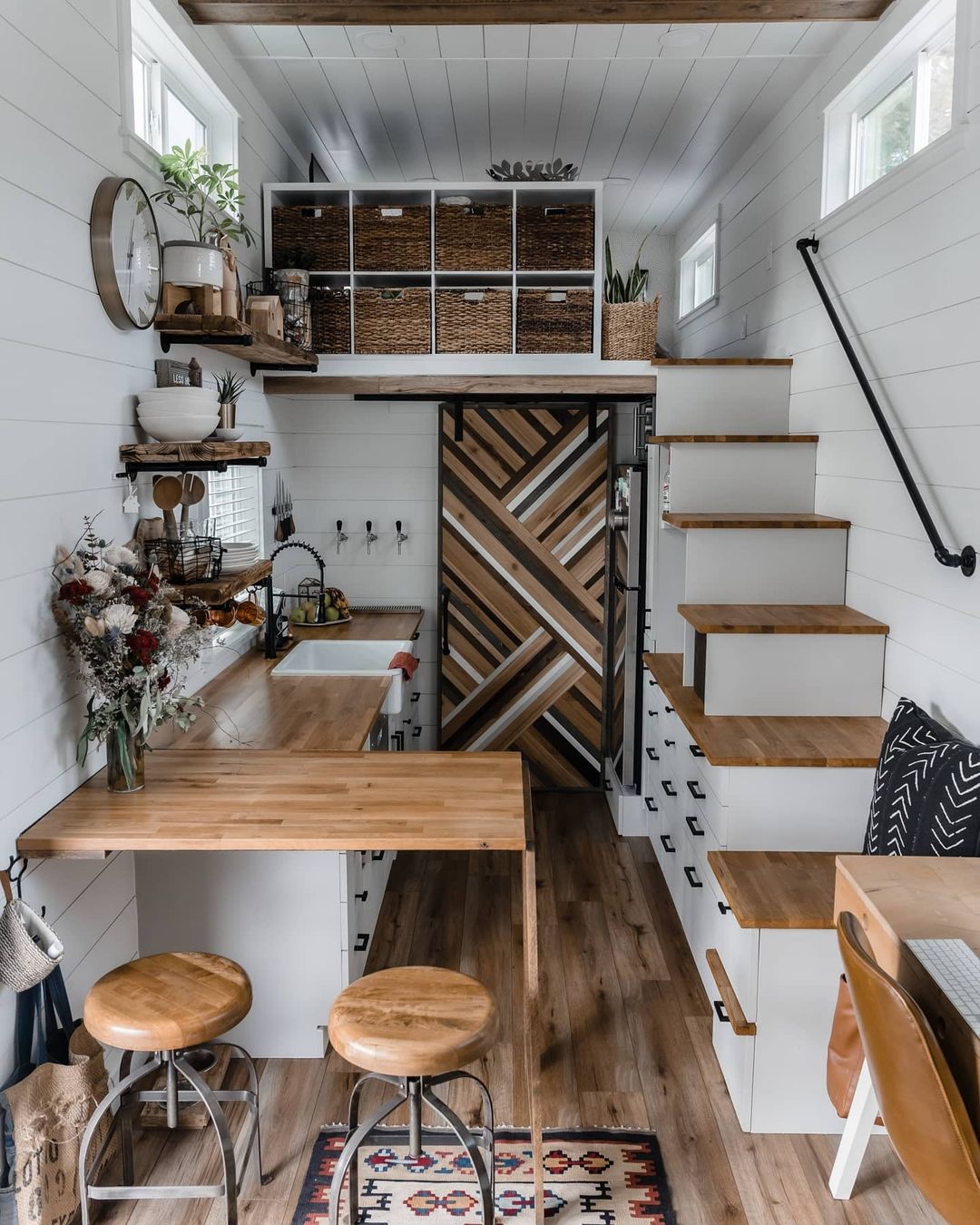 Interior of a shipping container home that includes a kitchen, staircase, and storage area. Photo by instagram user @tinyhomiez