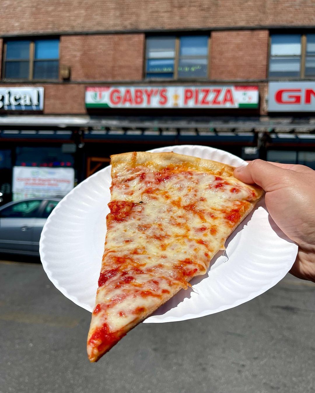 Slice of New York pizza in front of Gaby's Pizza in Queens photo by instagram user @nycpizzareview