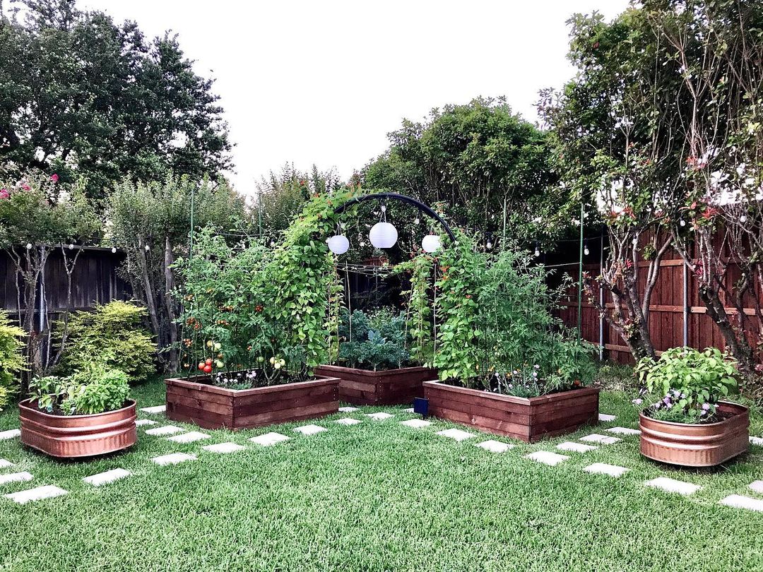 Manicured lawn with a stone walkway and several wooden raised garden beds and a pergola with vines. Photo by instagram user @thekiwihome