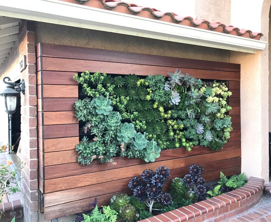 Succulent wall inserted into wood over a raised garden bed made out of brick. Photo by instagram user @greenwallmojo