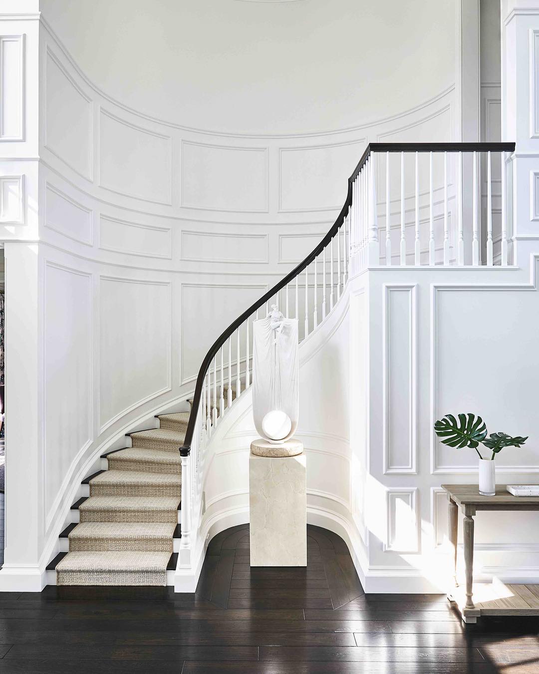 White entryway with a winding staircase and dark wood floors and features. Photo by instagram user @gazette_peninsula