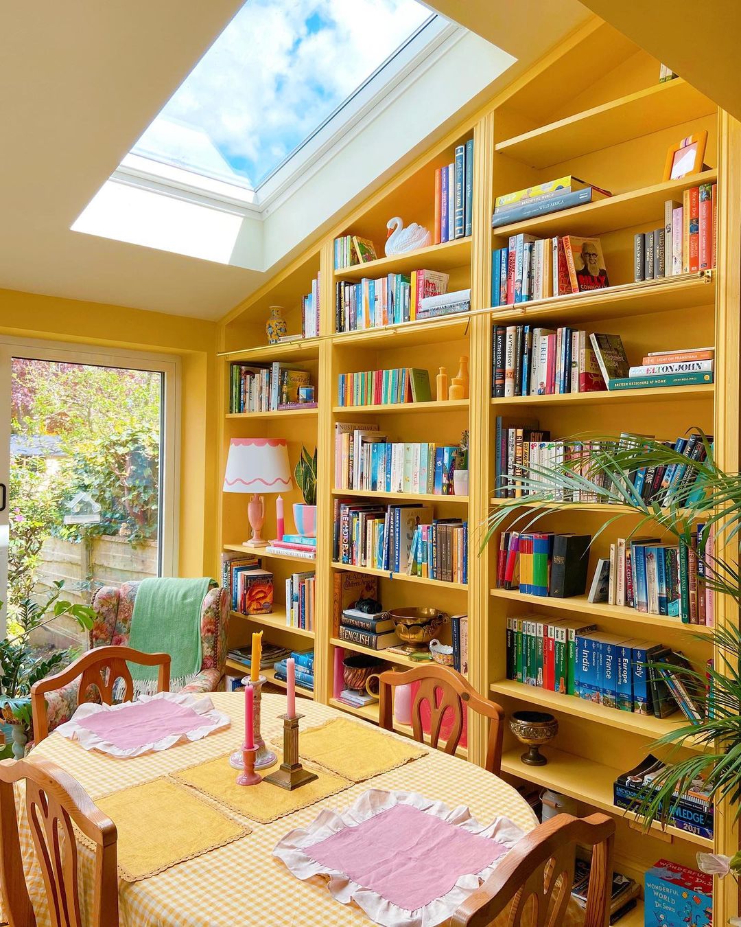 Yellow kitchen table near a yellow bookshelf with colorful books and a skylight. Photo by instagram user @thepaintspotcos