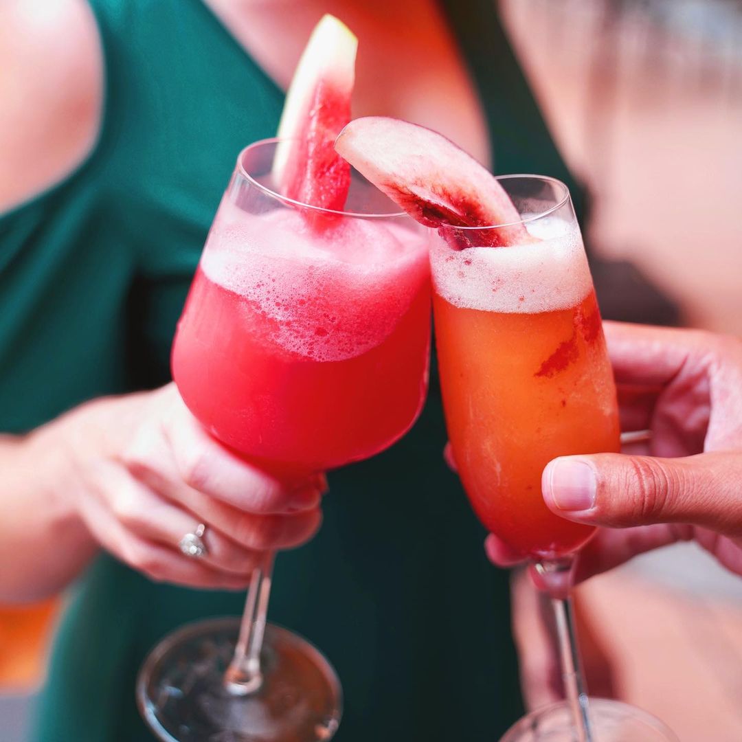 Two people clinking cocktail glasses with alcoholic fruit drinks. Photo by Instagram user @lobbyriverside.