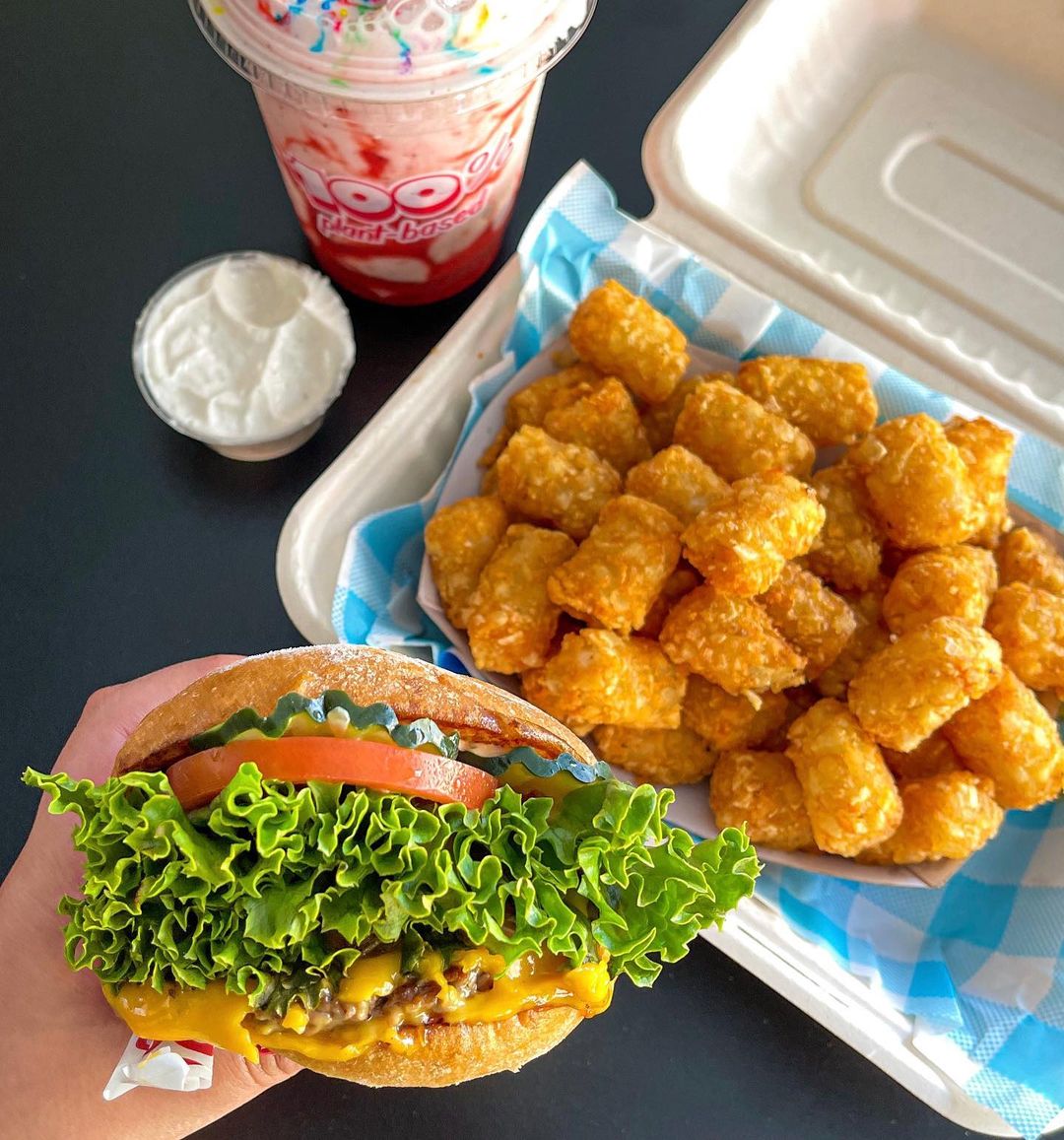 Delicious-looking impossible cheeseburger photoed with tater tots and a fruit-based smoothie. Photo by Instagram user @itsairamsveganvida.