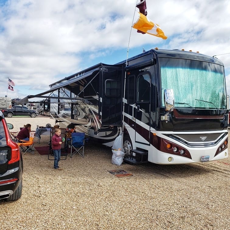 Large recreational vehicle during a tailgating party with a team flag attached and people under an awning. Photo by instagram user @american_dream_vacations