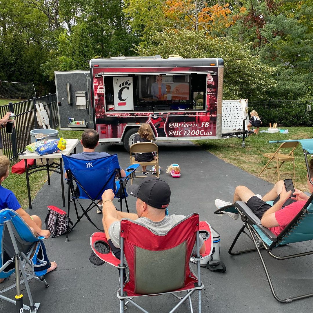 People sitting in front of a converted tailgating trailer watching a game on the TV. Photo by instagram user @saoyler