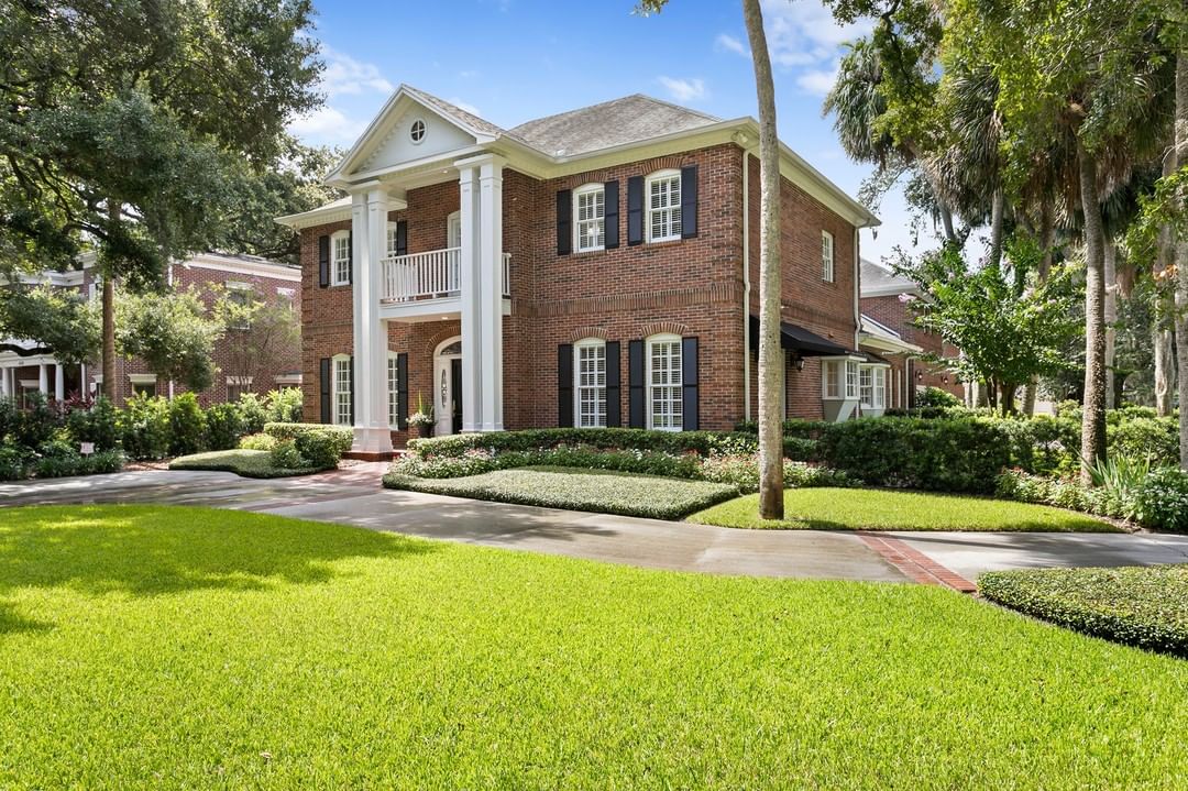 Large brick colonial house with a landscaped yard and white pillars with a balcony. Photo by instagram user @tonysicaphotography