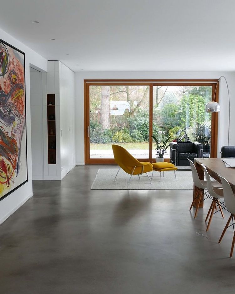 Open modern home floor plan with a large glass window and gray concrete floors with a statement chair. Photo by instagram user @danwheelersellshomes