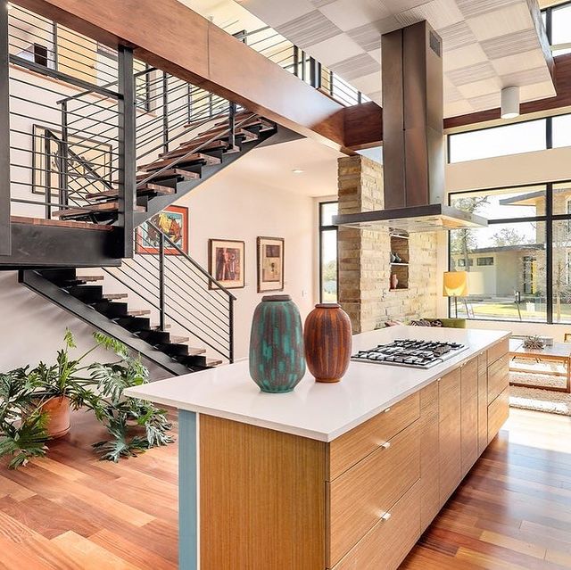 Staged modern kitchen with an open floor plan, wooden cabinets and floors, and a steel staircase. Photo by instagram user @starlight_village_homes