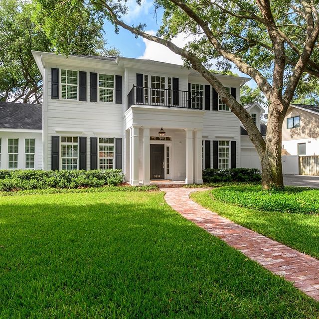 Colonia style white home with a lot of windows with black shutters and pillars surrounding the front porch. Photo by instagram user @middlebayhomes