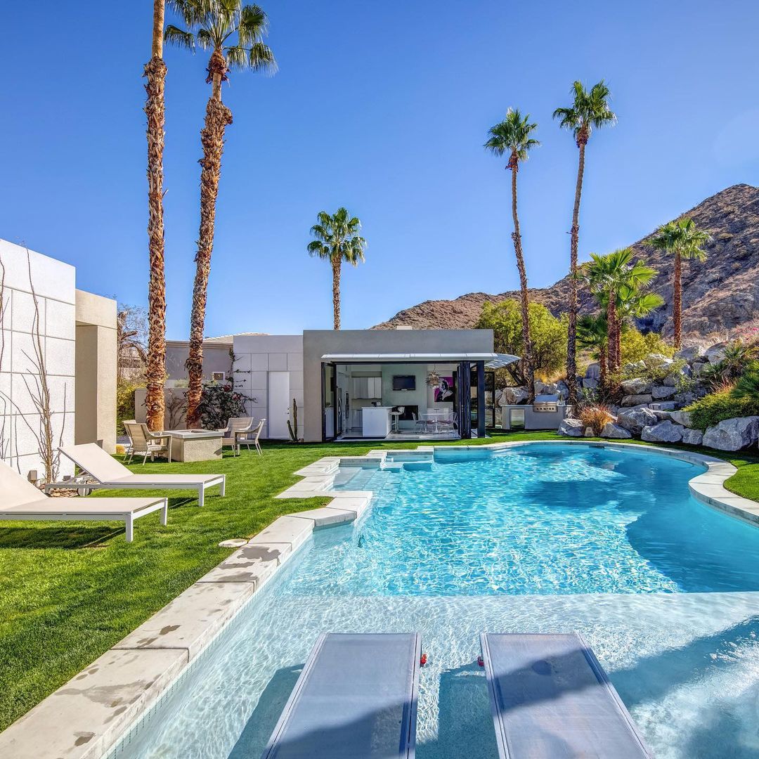 The back yard of a modern home with palm trees surrounding a large luxury pool. Photo by instagram user @bradysandahlrealestate